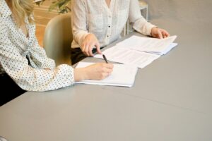 une femme signant sur du papier d'imprimante blanc à côté d'une femme sur le point de toucher les documents