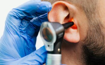 Gros plan d'un médecin utilisant un otoscope pour examiner l'oreille d'un patient dans un contexte clinique.