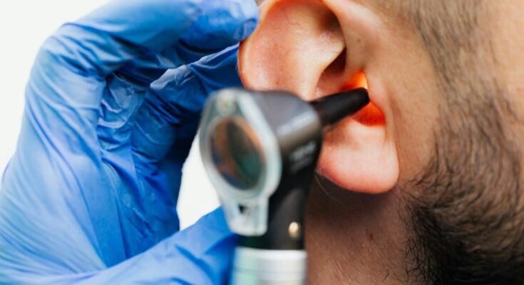 Gros plan d'un médecin utilisant un otoscope pour examiner l'oreille d'un patient dans un contexte clinique.