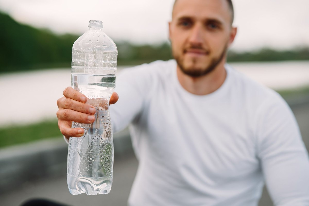 Homme tenant une bouteille d'eau près d'un corps d'eau