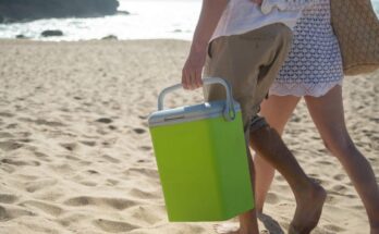 Homme et femme marchant sur la plage, le premier transporte un cooler vert