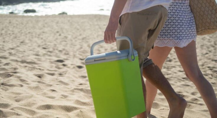 Homme et femme marchant sur la plage, le premier transporte un cooler vert