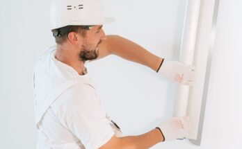 Un ouvrier en tenue blanche installe une plaque sur un mur blanc