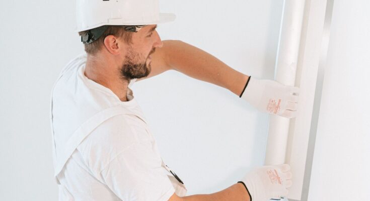 Un ouvrier en tenue blanche installe une plaque sur un mur blanc