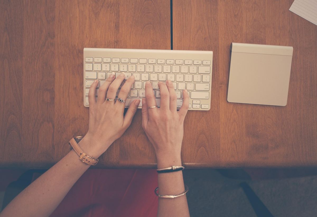 Une personne tape sur un clavier blanc, sur un bureau en bois